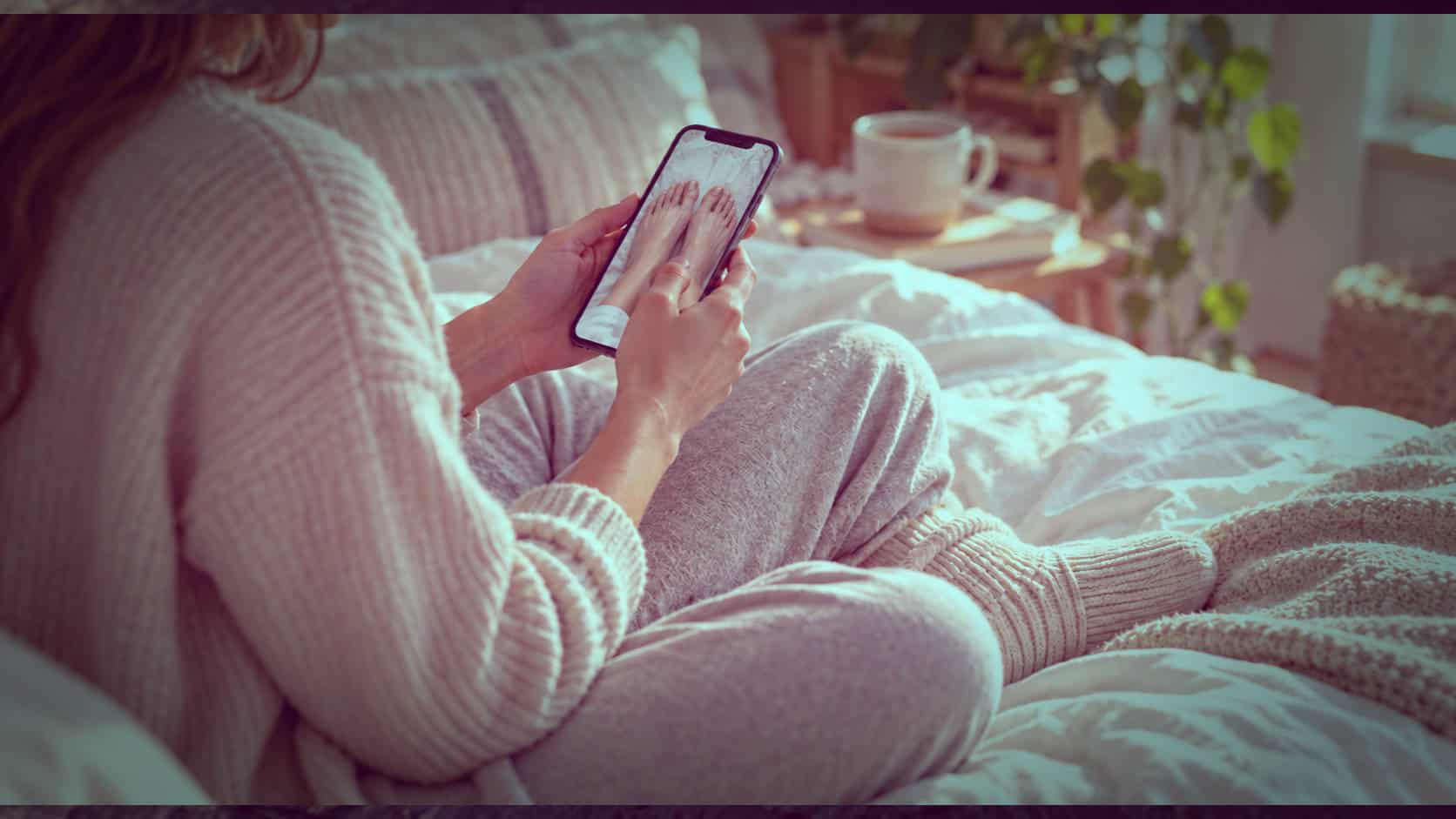 Person sitting on a bed in cosy socks, taking a photo with a smartphone