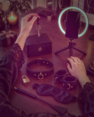Adult creator holding a key beside a ring light, lockbox and BDSM accessories.